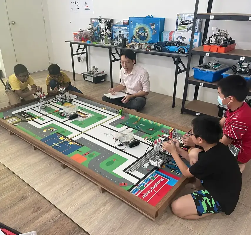 Advaspire students building and testing LEGO robots on a competition mat while a coach scores their run