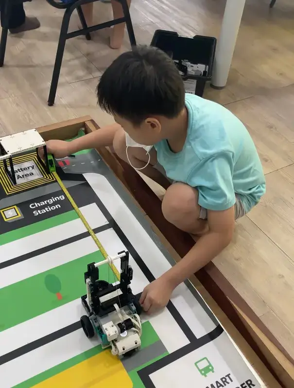 A student measuring his robot against the mat with a tape before changing his code