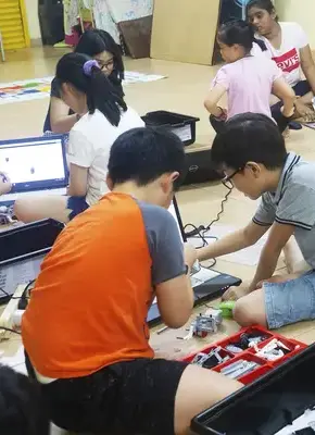 many students with group of 2 sitting on floor doing lego robotics and let the robot move