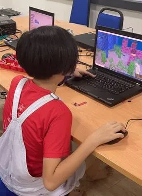 a Chinese little girl with red cloth using laptop to learn Minecraft coding at Advaspire centre
